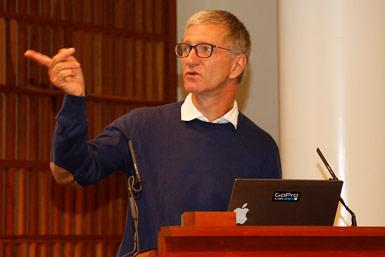 Professor Olaf Riess från Solve-RD i Tübingen pekar medan han presenterar vid ett podium med en uppfälld bärbar dator.