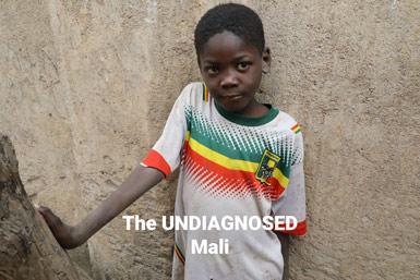 En pojke i färgglatt randig tröja lutar sig mot en stenmur, med texten The UNDIAGNOSED Mali.