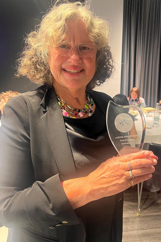 Helene Cederroth smiles while holding the glass Aurora Awards 2024 trophy from Rare Diseases International.