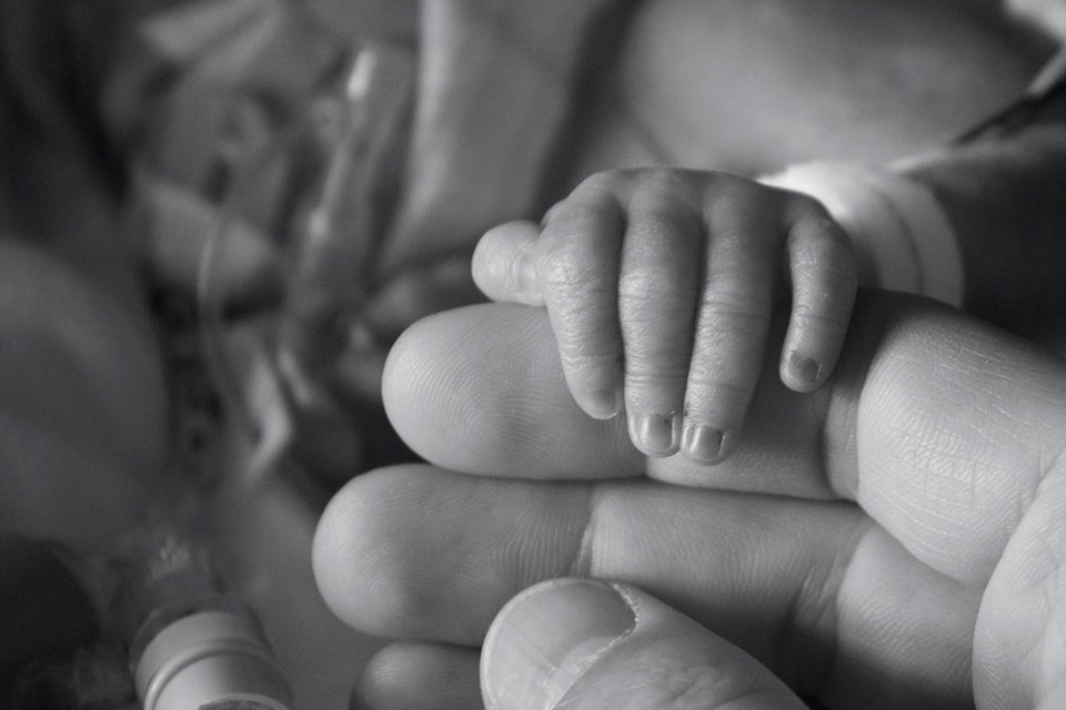 A prematurely born little baby holds his little hand around one of dad's fingers.