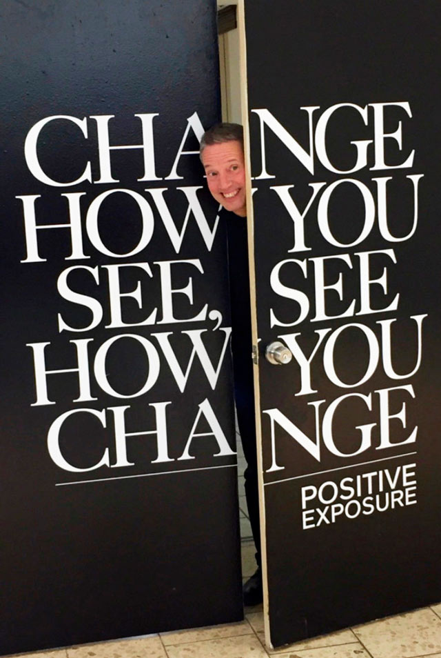 A man looks up behind a double door with the text CHANGE HOW YOU SEE, SEE HOW YOU CHANGE.